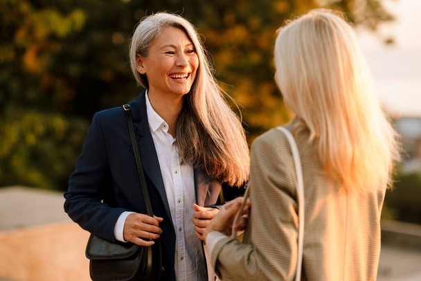 Mature multiracial businesswomen smiling and talking during meeting outdoors - Фото, изображение