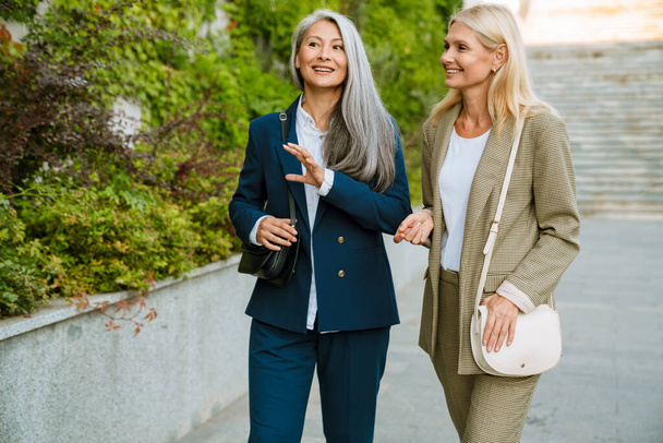 Mature multiracial businesswomen smiling and talking during walking outdoors - Zdjęcie, obraz