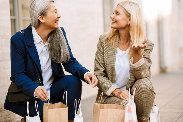 Mature multiracial women smiling while talking about their shopping outdoors - Foto, Imagem