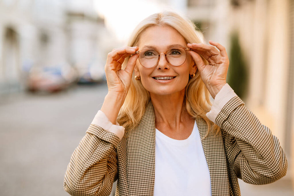 Mature white woman wearing eyeglasses smiling and looking upward outdoors - Fotoğraf, Görsel