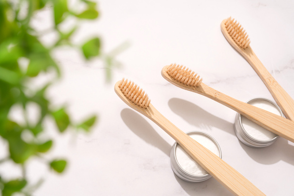 Doğal ahşap bambu diş fırçaları ve mineral diş tozu beyaz masa arkasında metal kaplarda kaolin. Doğal banyo ürünleri, organik diş fırçası. Model görüntüsü. Üst görünüm - Fotoğraf, Görsel