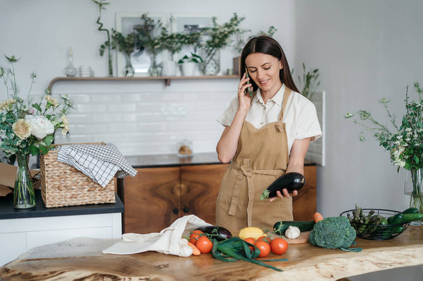 Young woman with mobile phone in kitchen cooking healthy vegan meal vegetables - Photo, Image