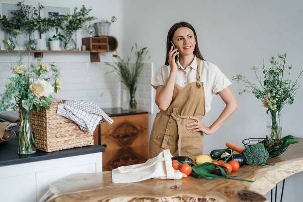 Jonge vrouw met mobiele telefoon in de keuken koken gezonde veganistische maaltijd groenten - Foto, afbeelding