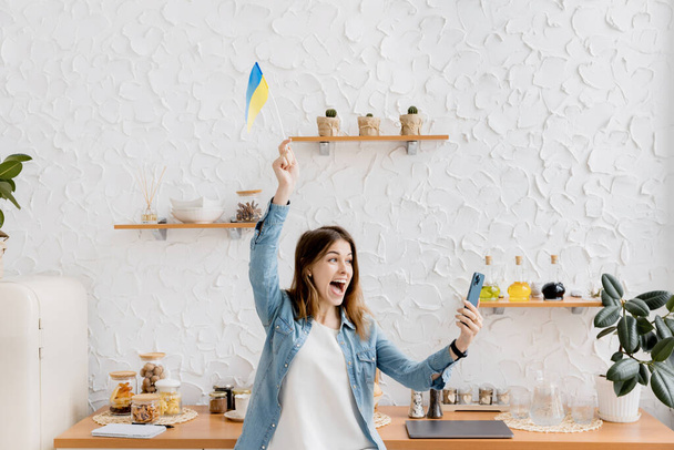 Boldog fiatal nő zászló Ukrajna segítségével smartphone - Fotó, kép