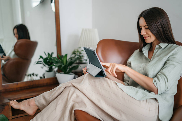 Fiatal nő dolgozik egy touchpad, úgy érzi, kényelmes otthon iroda egy zöld növény a háttérben - Fotó, kép