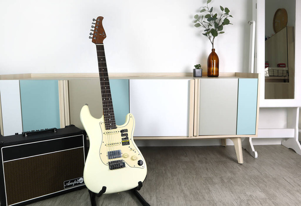 vintage white color electric guitar brand GTRS and Amppro amplifier speaker are on the wooden floor in the minimal design living room during new year pary with family in evening - Valokuva, kuva