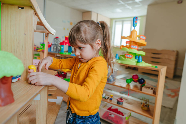 Маленька дівчинка грає з дерев'яним будинком з іграшковими меблями в дитячому саду або дитячому центрі. Ранній розвиток з іграшками з натурального матеріалу. Концепція освіти Монтессорі
. - Фото, зображення