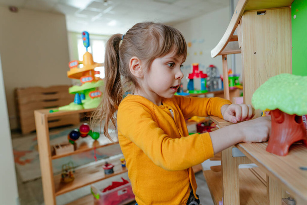Pikkutyttö leikkii puutalolla leluhuonekaluilla päiväkodissa tai lastentarhassa. Varhainen kehitys luonnon materiaali leluja. Montessori koulutuksen käsite. - Valokuva, kuva