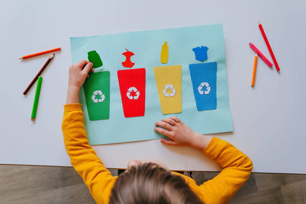 幼稚園や小学校で分別用のゴミ入れのポスターで遊んでいる女の子。リサイクル教育の考え方. - 写真・画像