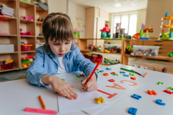 Bambina che scrive una parola CAT giocando con lettere di plastica colorate all'asilo o alla scuola primaria. Metodi tattili e sensoriali per l'apprendimento. Concetto educativo. - Foto, immagini