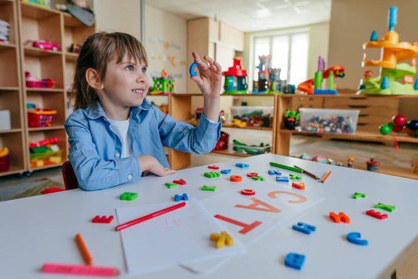 Little girl writing a word CAT playing with colorful plastic letters at kindergarten or primary school. Tactile and sensory methods for learning. Education concept. - Фото, зображення
