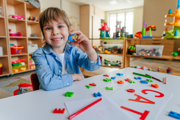Kleines Mädchen, das im Kindergarten oder in der Grundschule mit bunten Plastikbuchstaben ein Wort schreibt. Taktische und sensorische Methoden zum Lernen. Bildungskonzept. - Foto, Bild