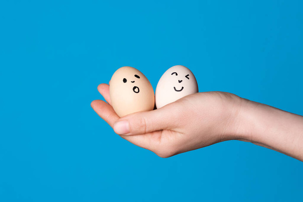 Mão segurando dois ovos de Páscoa com uma cara engraçada desenhada nele. Conceito de alimentação de Páscoa ou dieta saudável - Foto, Imagem