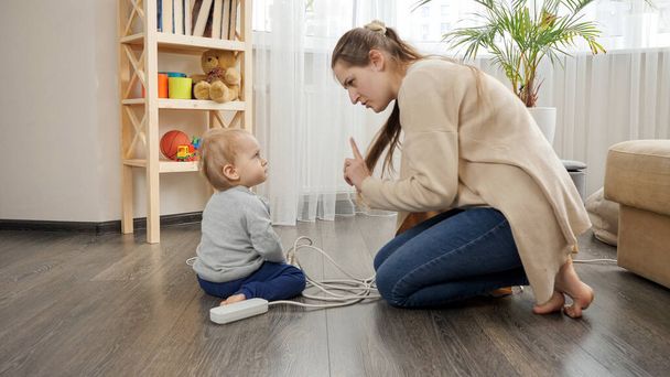 jong zorgzame moeder vertellen haar baby zoon niet te spelen met elektriciteit - Foto, afbeelding