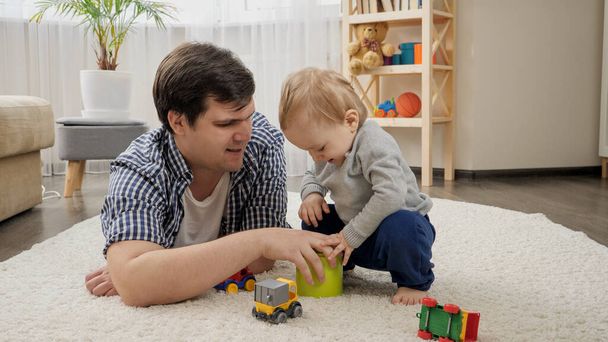 Little baby boy giving toys to his father for playing on carpet. - 写真・画像