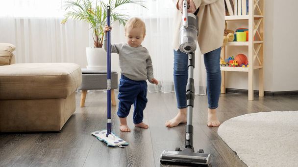 Mały chłopiec pomaga matce sprzątać w domu i odkurzać dywan.. - Zdjęcie, obraz
