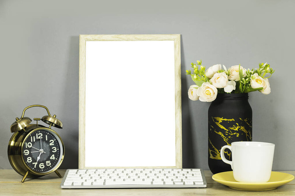 still life: empty picture frame mockup and flowers vase and cup of coffee and alarm clock, keyboard on wooden desk table. Elegant working space, home office concept - Photo, Image