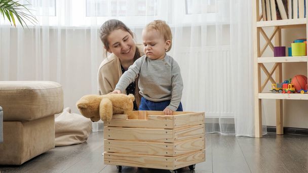Niño pequeño con madre recogiendo juguetes en caja de juguetes de madera en la sala de estar - Foto, Imagen
