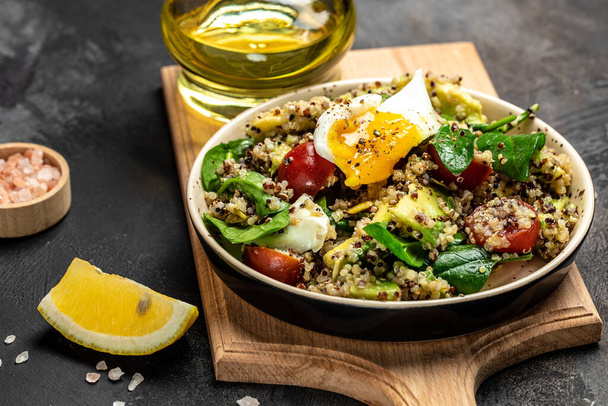 Keto diétás quinoa, avokádó, tojás, paradicsom, spenót és napraforgómag sötét alapon. Egészséges ételek, ketogén étrend, diétás ebéd koncepció, élelmiszer recept háttér. Közelről.. - Fotó, kép