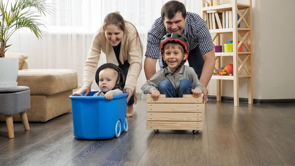 Famiglia felice giocando a casa e avendo gara in carrelli con bambini - Foto, immagini