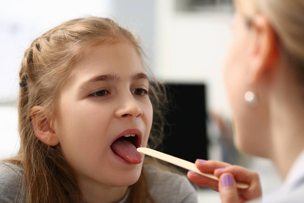 Pediatrician checking girls hurting throat with stick - Foto, imagen