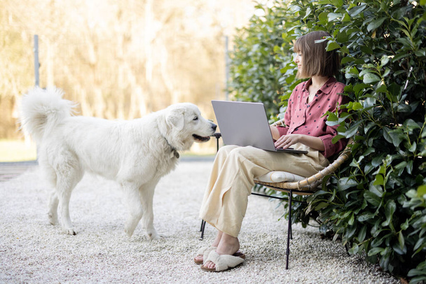 Frau arbeitet am Laptop, sitzt mit Hund im Garten - Foto, Bild