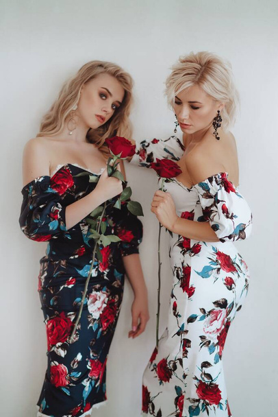 Beautiful young mother and her teenage daughter in identical dresses with roses on a light background. Happy motherhood. Teen parenting concept - Fotografie, Obrázek