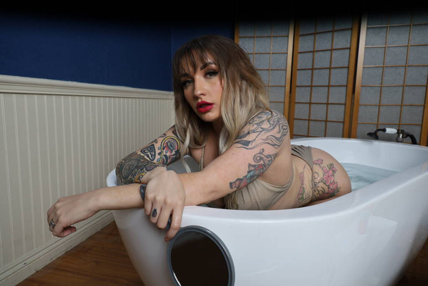 Photo of a beautiful white model sitting in a tub looking in a mirror - Valokuva, kuva