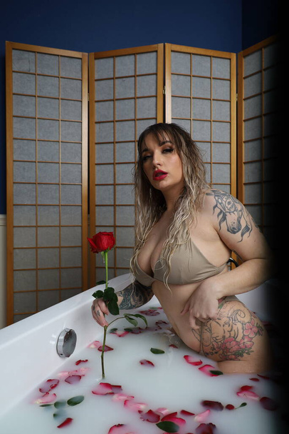 Photo of a beautiful white model sitting in a tub with milk water and rose petals - Valokuva, kuva