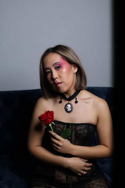 Photo shoot of a beautiful Vietnamese model holding a rose, and sitting on a couch - Zdjęcie, obraz