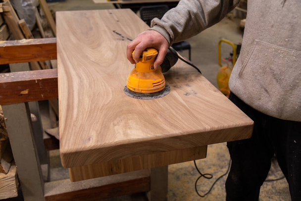 Closeup of carpenter sanding wood table with orbital sander in a workshop - Photo, Image