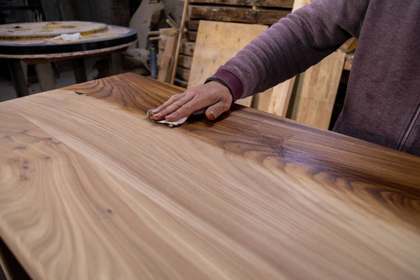 Крупним планом тесля покриває дерев'яний стіл захисною лляною олією. Процес виготовлення дерев'яного столу
 - Фото, зображення