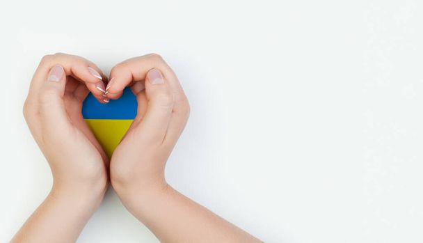 Female hand holding heart with Ukrainian flag on white background. Love Ukraine concept - Valokuva, kuva