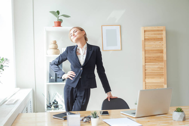 Positive beautiful business woman standing indoors in office, relaxing and enjoying the spring sun by the window - Foto, Imagem