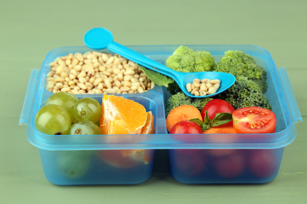 Вкусная вегетарианская еда в пластиковой коробке на зеленом деревянном столе
 - Фото, изображение