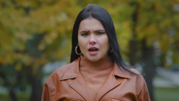 Headshot close-up young attractive worried sad hispanic woman standing outdoors shocked by negative news upset feeling shock experiencing anxiety thinking about problem nervous keeps hand on face - Footage, Video