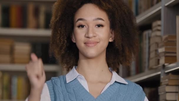 Fejlövés boldog női hallgató áll az egyetemi könyvtár mosolyog a kamera mutatja hüvelykujj fel gesztus jóváhagyása élvezi a főiskolai tanulmányok sikeres tanulmányi minőségű felsőoktatási ösztöndíj - Felvétel, videó