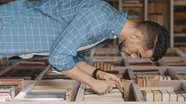 Fiatal jóképű szakállas indiai férfi diák egyetemi könyvtár vagy könyvesbolt választ könyvet könyvespolcon keresi a megfelelő tankönyvet tantárgy felsőoktatási koncepció függőleges formátum videó - Felvétel, videó