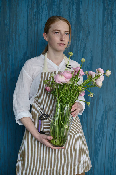 portrait of a young beautiful florist on a blue background with a bouquet in his hands - Valokuva, kuva