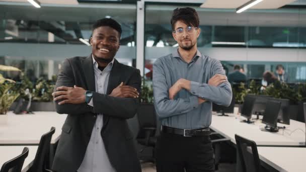 Multiracial pareja de colegas de negocios sonriendo diversos compañeros de trabajo árabe joven africano gerente hombre de negocios chico de pie en el interior posando juntos cruzando brazos mirando la cámara en el lugar de trabajo de la oficina - Imágenes, Vídeo