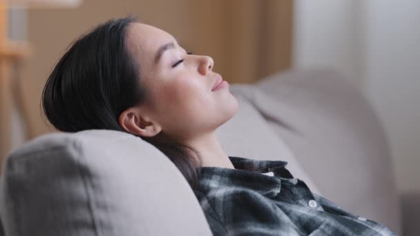 Side view close up Asian calm woman relaxed Korean lady in checkered casual shirt close eyes resting sleep on back of couch relaxing dreaming on comfortable sofa in living room at home lazy time - Footage, Video
