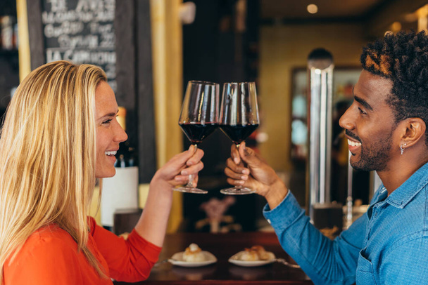 interracial couple smiling as they toast with glasses of red wine - Valokuva, kuva