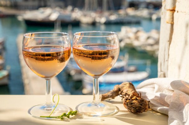 Festa de verão com rosa fria Vinho provençal em vidro servido em luzes solares no terraço ao ar livre com vista para o antigo porto dos pescadores com barcos coloridos em Cassis, Provence, França - Foto, Imagem