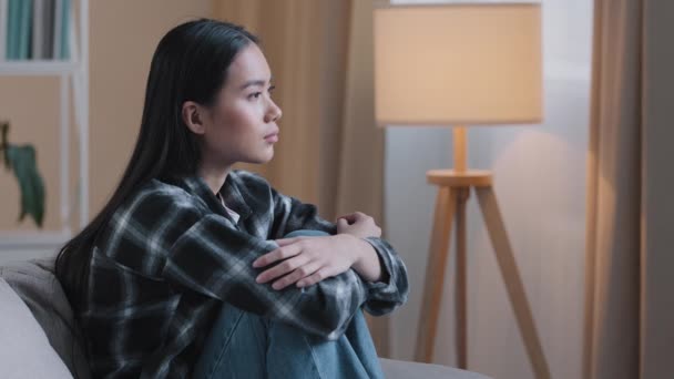Side view sad asian woman sitting on couch at home feeling unsure about hard decision unhappy bad feeling mental trouble sits on sofa. Depressed korean lady regretting mistake psychological trouble - Footage, Video