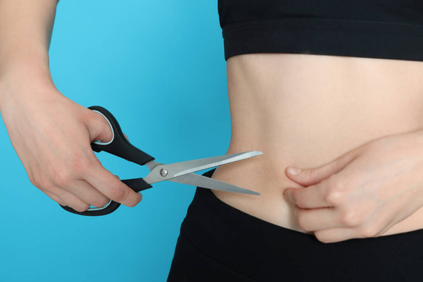 Slim woman with scissors on light blue background, closeup. Weight loss surgery - 写真・画像