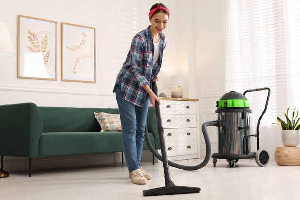 Young woman vacuuming floor in living room - Foto, imagen