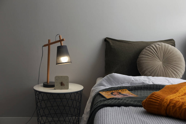 Стильная лампа и будильник на тумбочке в помещении. Элементы интерьера спальни - Фото, изображение