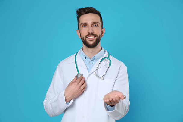Doctor with stethoscope holding something on light blue background. Cardiology concept - Foto, Imagen