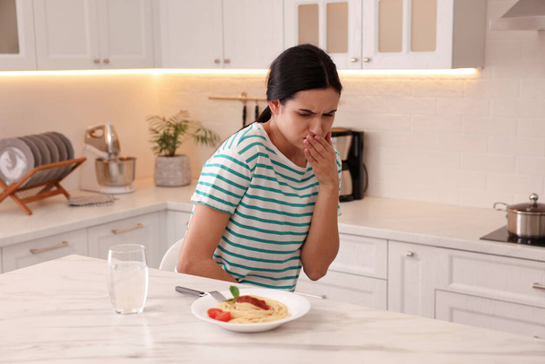 Young woman feeling nausea while seeing food at table in kitchen - Фото, зображення
