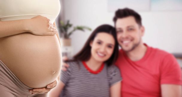 Leihmutterschaft. Junge schwangere Frau und verschwommener Blick auf glückliches Paar drinnen, Bannerdesign - Foto, Bild